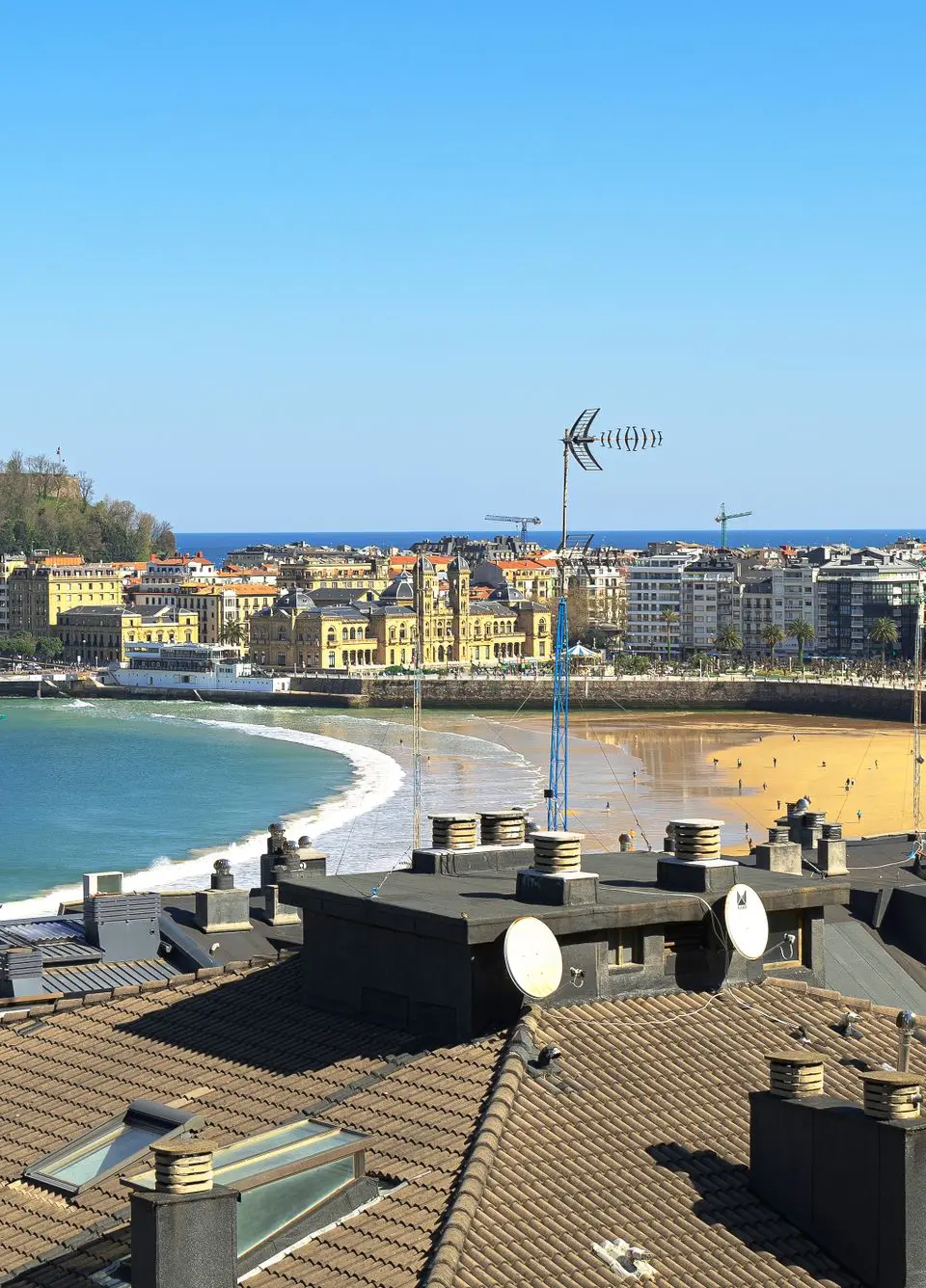 Expansive view over rooftops towards the beachfront of San Sebastián, showcasing cityscape and bay.