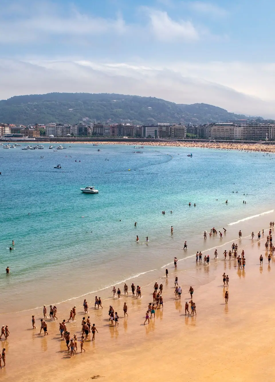 Crowds enjoy a bustling day at San Sebastián beach with clear sky and turquoise water.