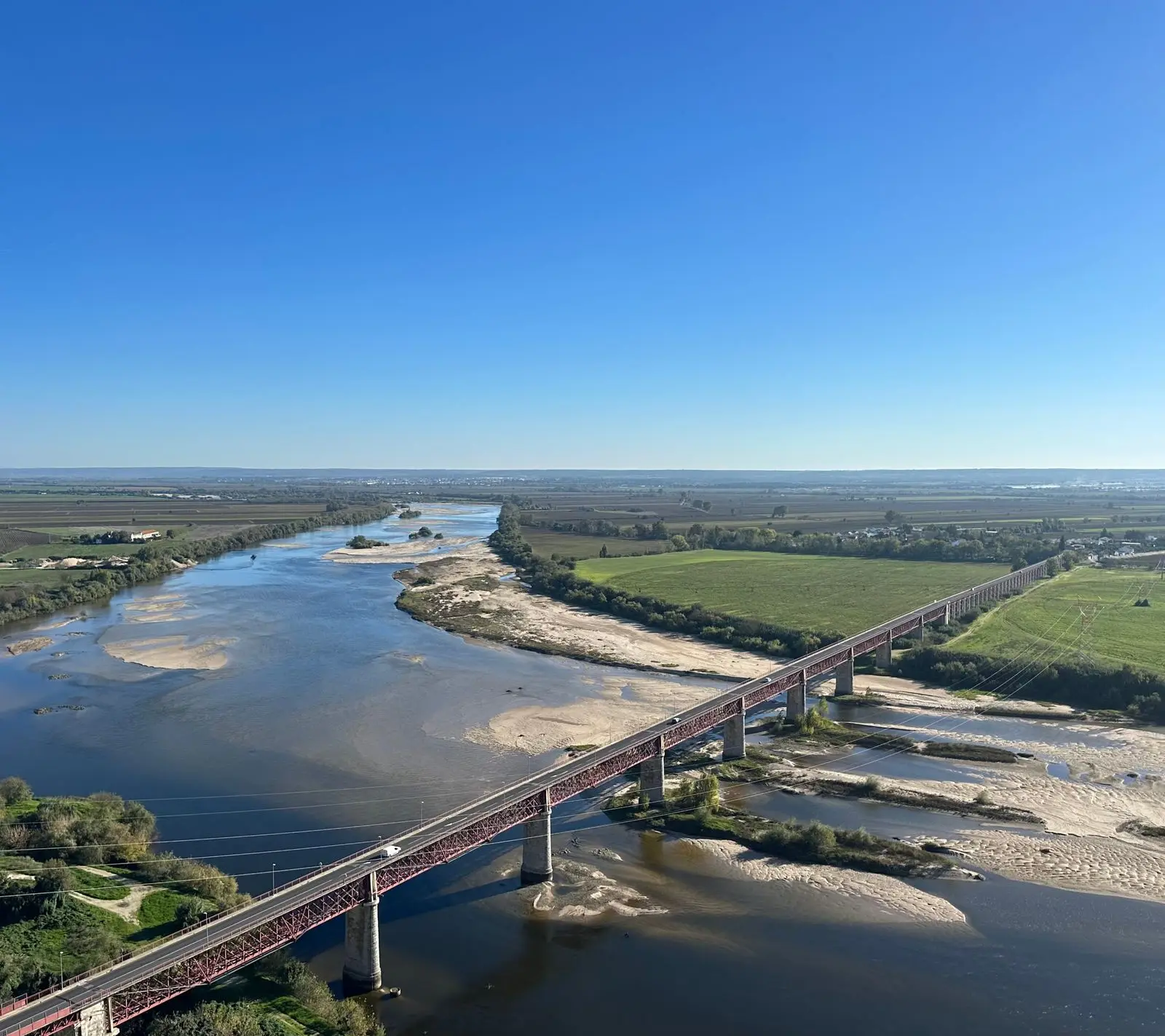 Stunning aerial view of a bridge spanning the Tagus River with lush green fields under a clear blue sky in Portugal.