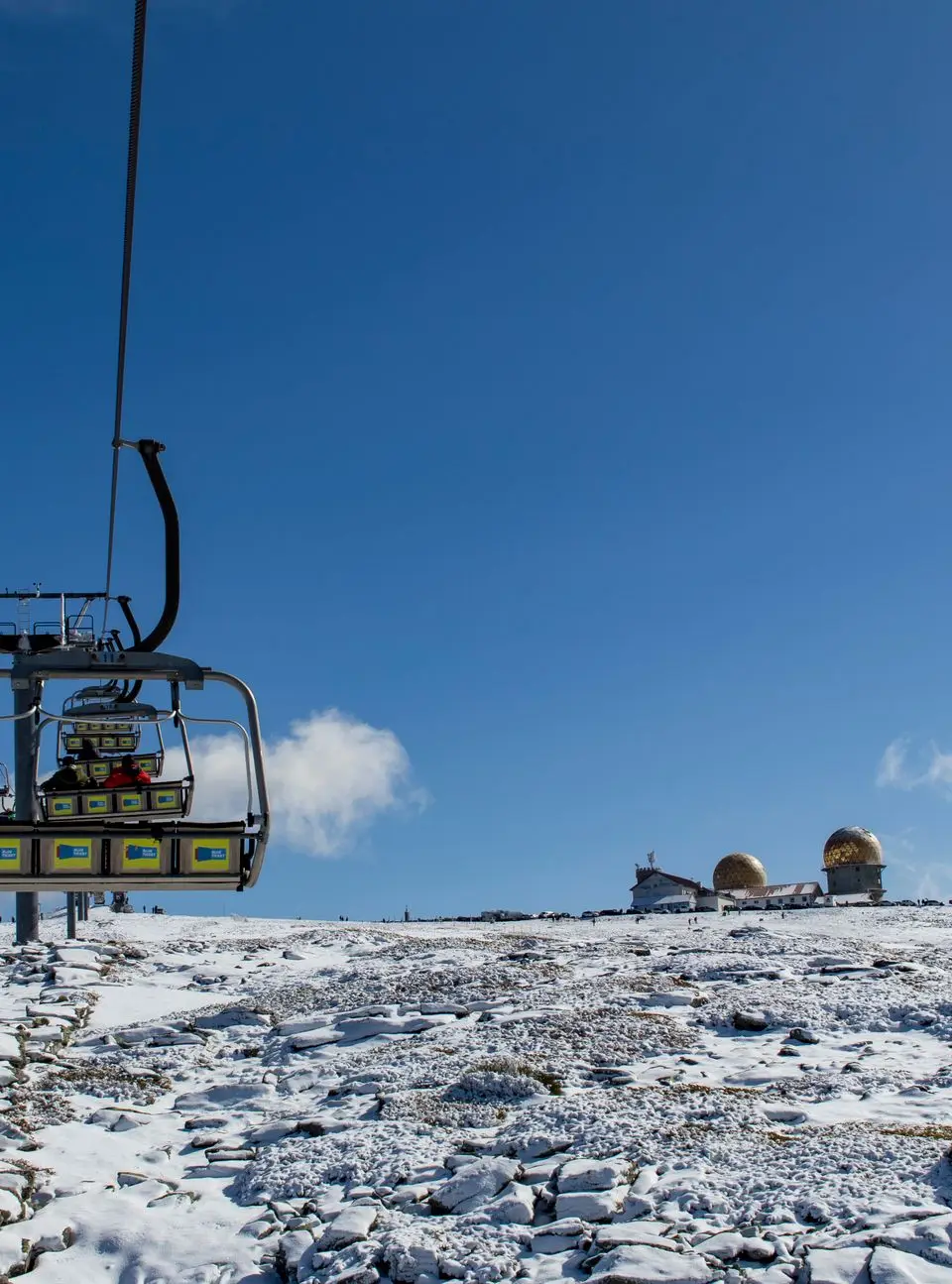Ski lift leading to a snow-covered plateau with observatory under a clear blue sky in Serra da Estrela.