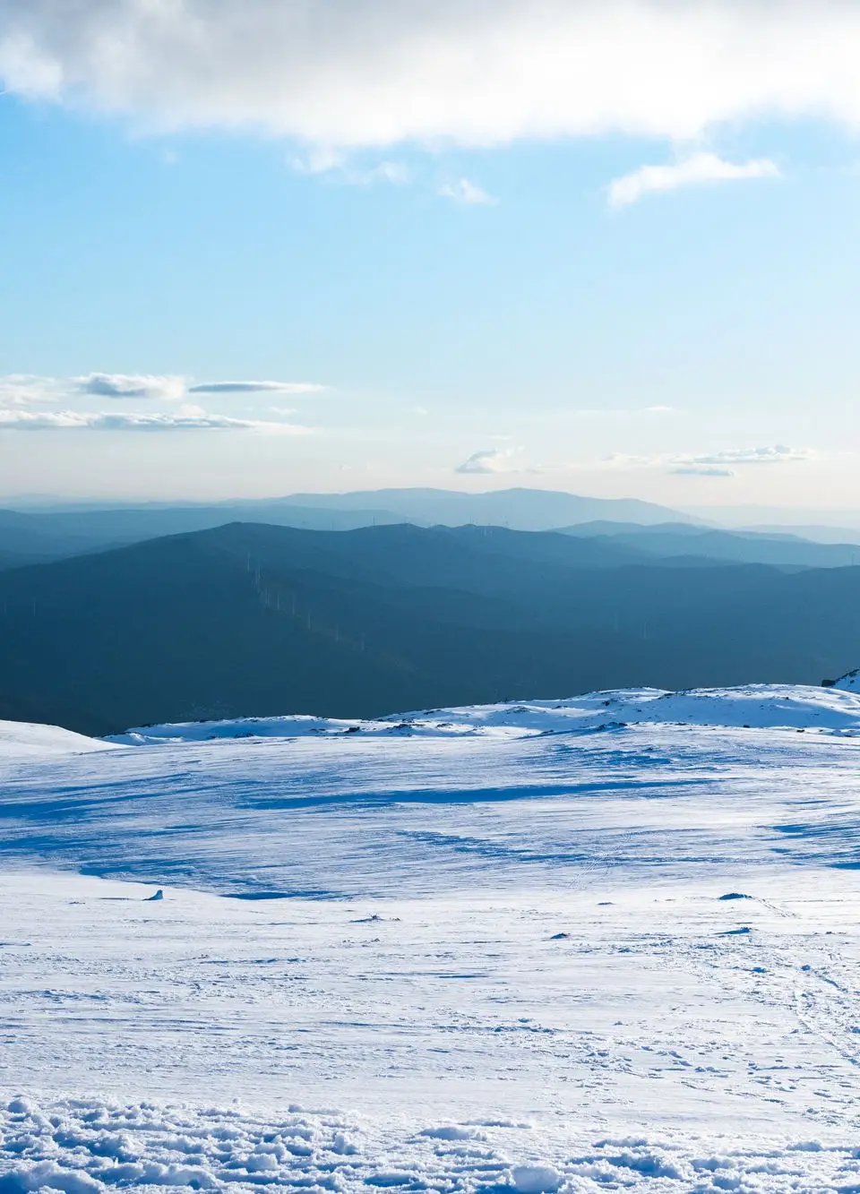 Vast snowy terrain with distant mountain views under a clear blue sky in Serra da Estrela, Portugal.