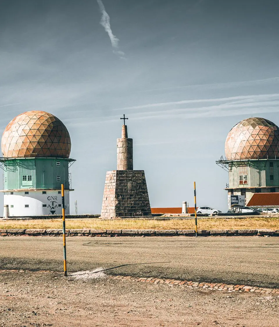 Radar towers and stone monument under clear skies in Serra da Estrela, Portugal.
