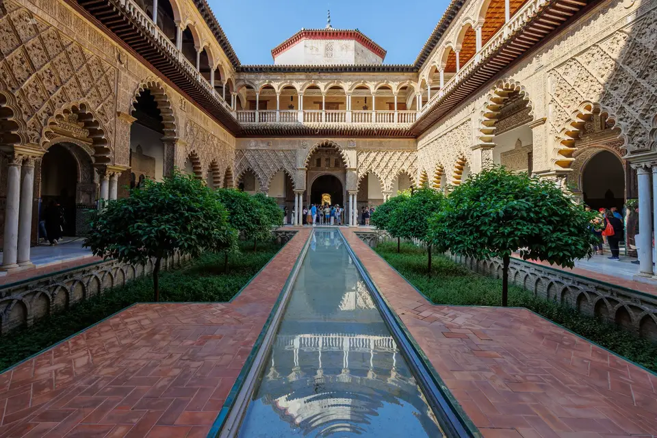 Explore the historic courtyard of Real Alcázar in Seville, showcasing stunning Moorish architecture and lush greenery.