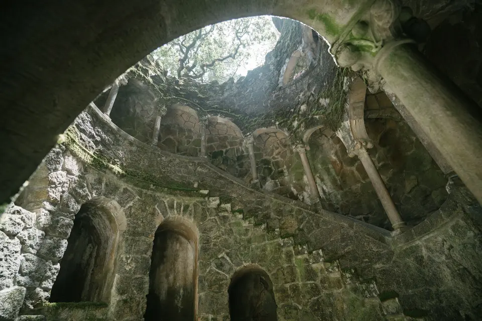 From below of dark moss grown Initiation Well with spiral staircase at Regaleira estate in Portugal