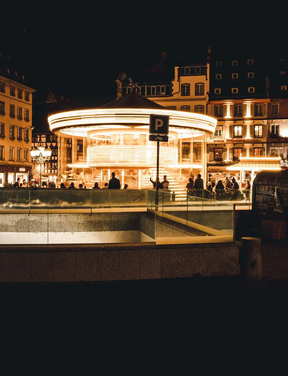 A vibrant night scene with illuminated carousel and historic buildings in Strasbourg, France.