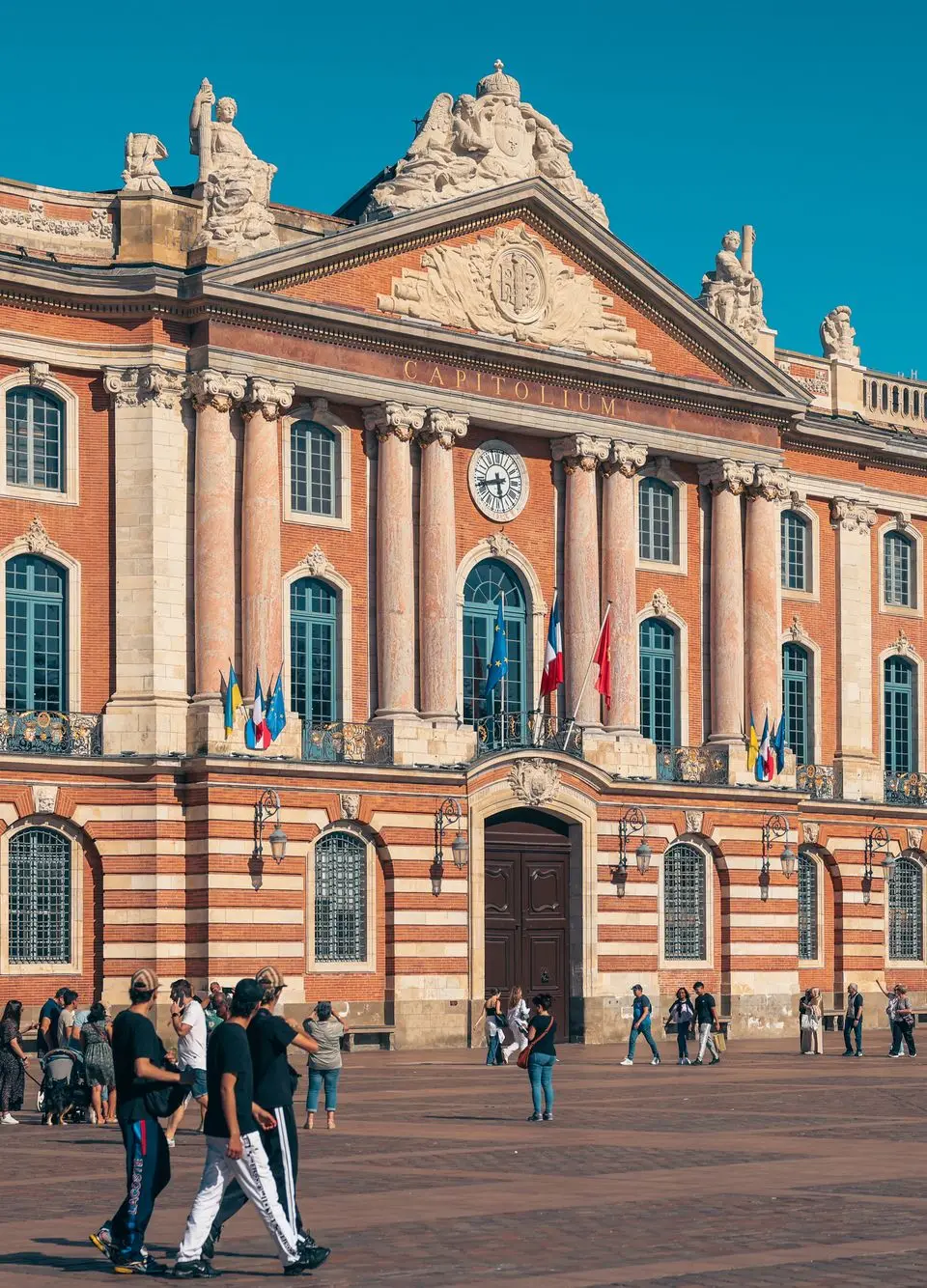 The iconic Capitole de Toulouse with people enjoying the sunny plaza in France.