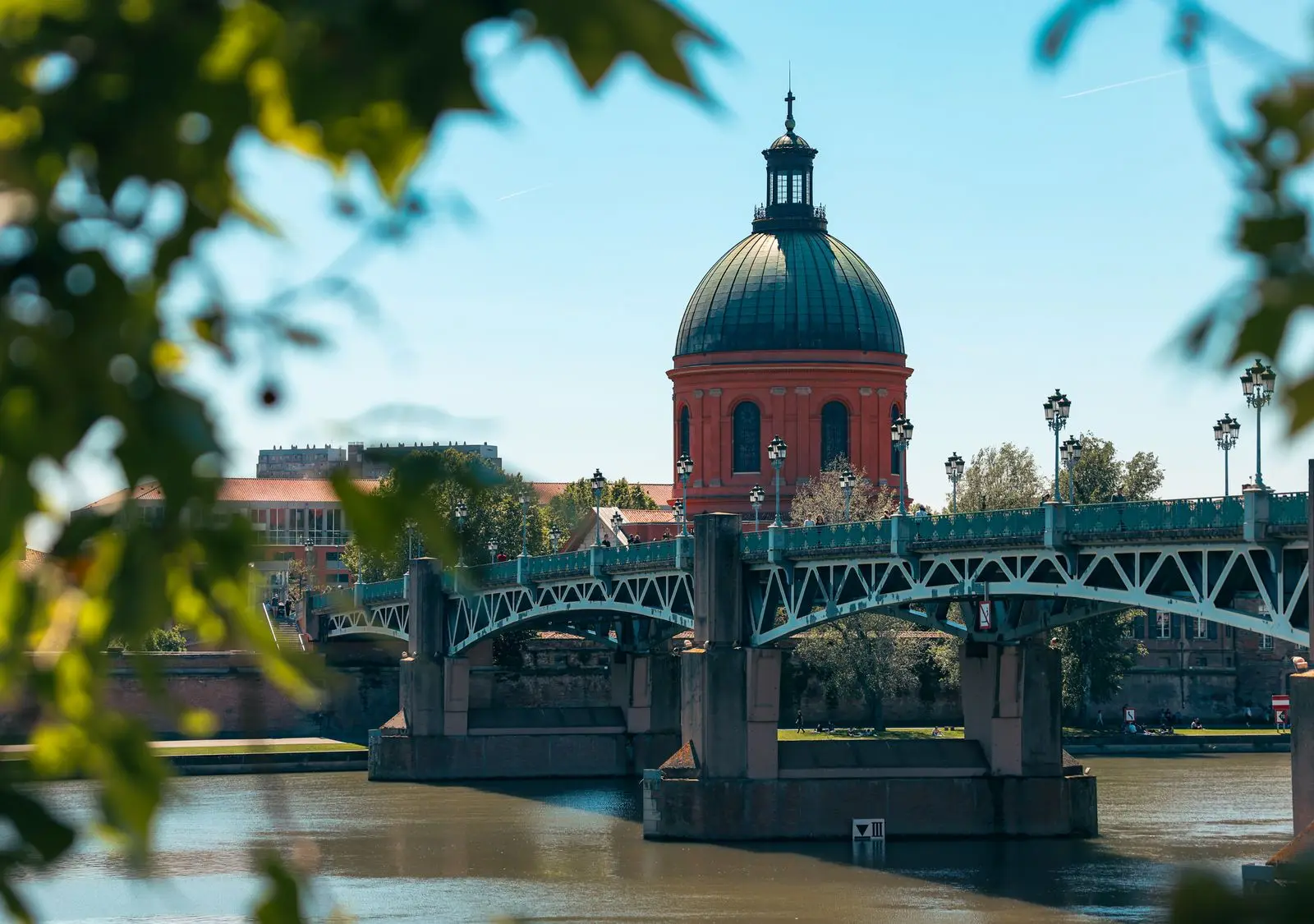Scenic view of Pont Saint-Pierre and red dome in Toulouse, France framed by leaves.