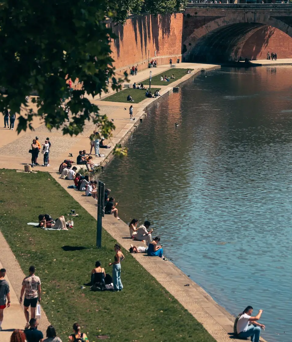 People relax by the Garonne River in Toulouse, enjoying the sunny day.