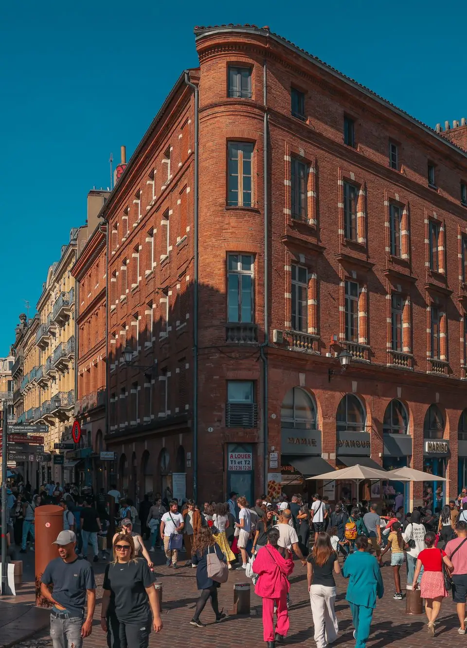 Vibrant street scene in Toulouse's historic district with crowds and red brick architecture.